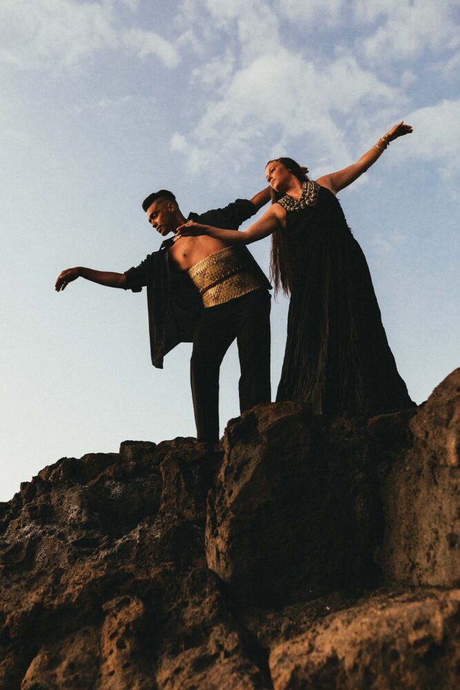 two people standing on rocks with arms outstretched, performing a hawaiian ceremonial dance