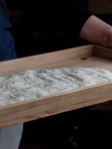 a person holding a wooden tray with white crystals